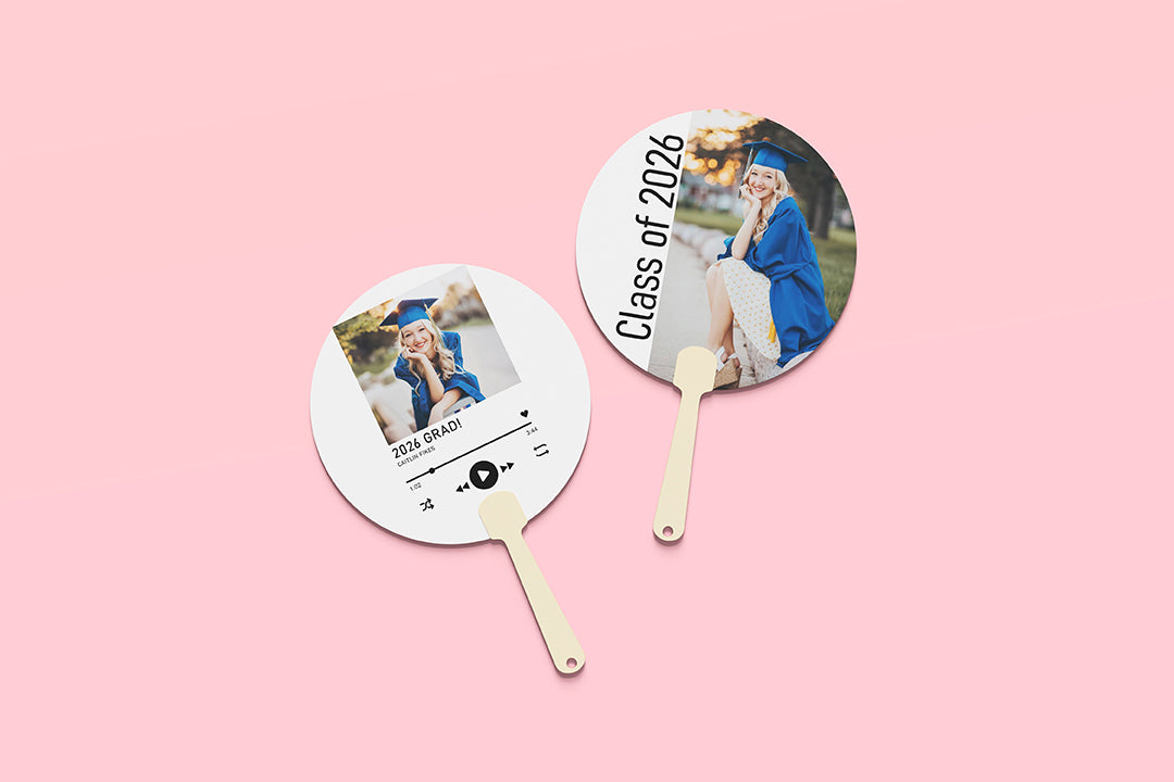 Two round fans with graduation-themed designs on a pink background